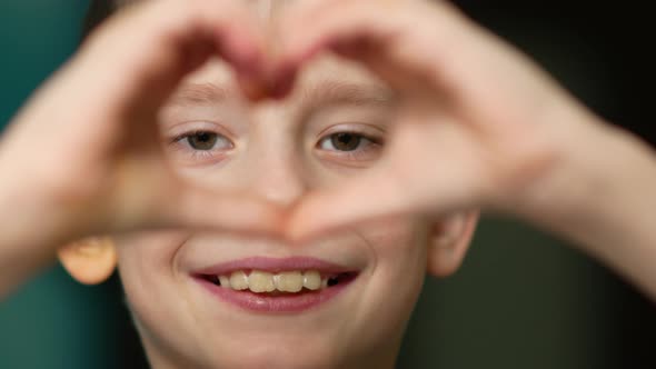Cute caucasian boy makes a heart-shaped gesture with his hands.