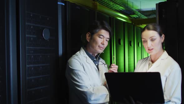 Diverse female and male it technicians in lab coats using tablet and laptop checking computer server