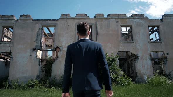 Young successful man in a jacket goes to an abandoned ruined house