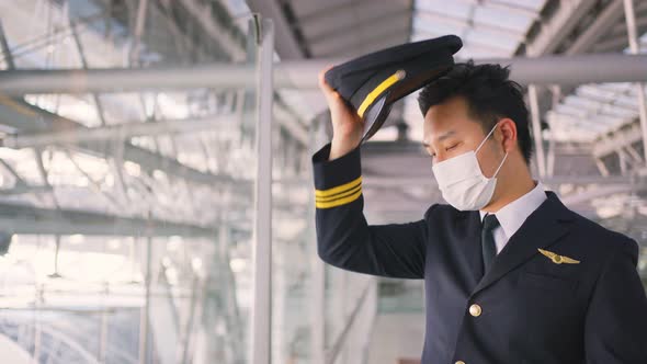 Airliner pilot wearing face mask walking in airport terminal and looking airplane with tired face.