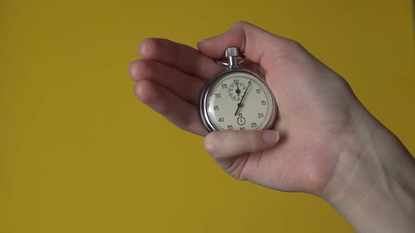 A woman's hand holds an analog stopwatch on a yellow background