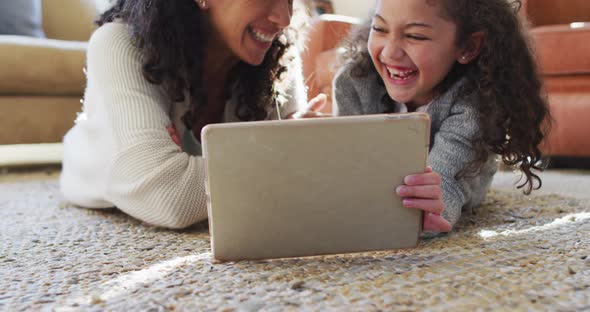 Happy mixed race mother and daughter laying on the floor,having fun and using tablet