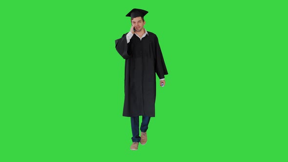 Male Graduate in Gown and Mortarboard Talking on the Phone While Walking with His Diploma