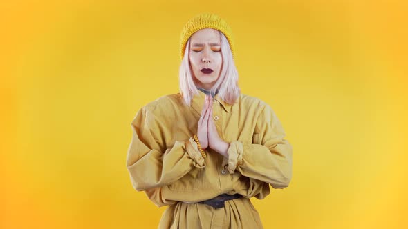 Cute Young Girl with Colorful Hairstyle Praying Over Yellow Background