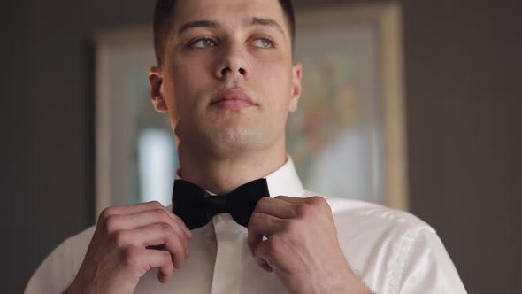 Groom Adjusts Bow Tie Preparing to Go to the Bride Businessman in White Shirt Wedding Day