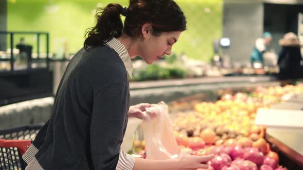 Young Beautiful Brunette Girl in Her 20's Picking Out Tangerines Into a Plastic Bag at the Fruit and