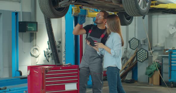 Mechanic Teaching Woman To Repair Car. Woman Learning and Noting or Filling in Document in Garage.