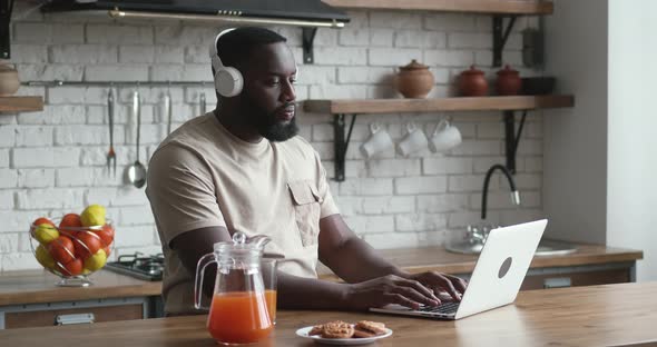 Freelancer Programmer in Headphones Working From Home on Kitchen and Using Laptop