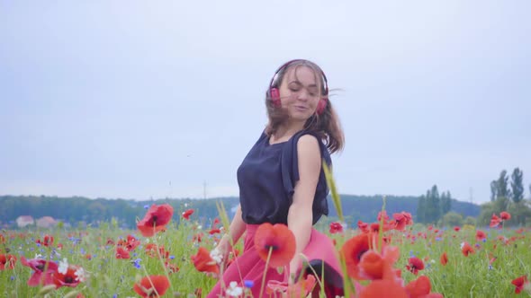 Cute Young Woman Wearing Headphones Listening To Music and Dancing in a Poppy Field Smiling Happily