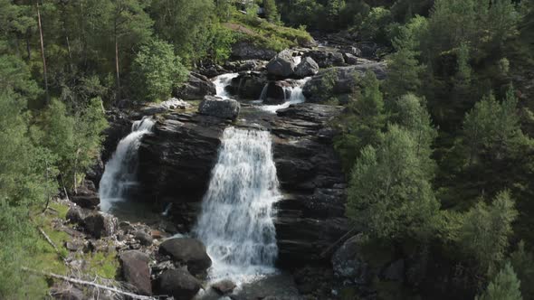 Aerial slowly flying forward over waterfalls rushing down hillside in evergreen forest