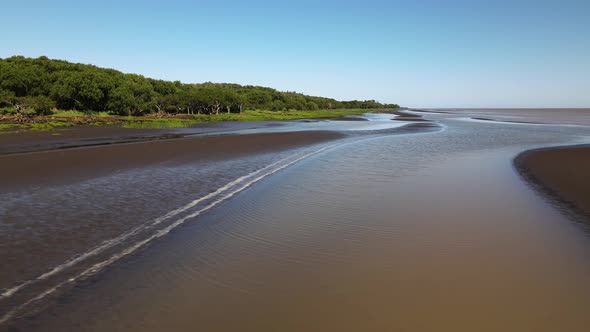 Low aerial pan of brown sand banks and swamp by Rio de la Plata coast