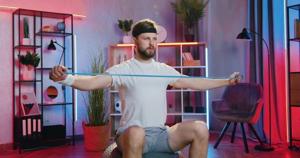 Guy in Sportswear Sitting on Fitball at Home in the Evening and Doing Exercises