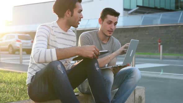 two young multiethnic men sitting outdoor using digital tablet and personal computer