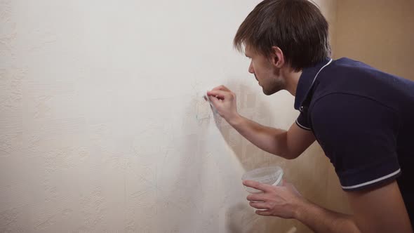 Caucasian Man Wipes Clean Children Drawing with Beige Grooved Wallpaper