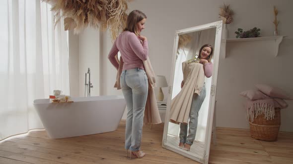 Elegant Charming Adult Woman Choosing Stylish Dress in Front of Mirror Indoors