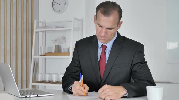 Middle Aged Businessman Writing Documents in Office