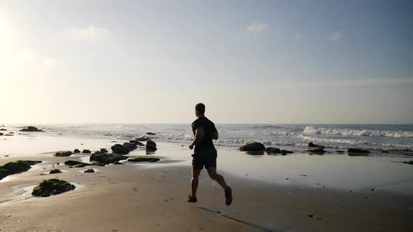 A strong man in silhouette running and fitness training on the beach at sunrise in Santa Barbara, Ca