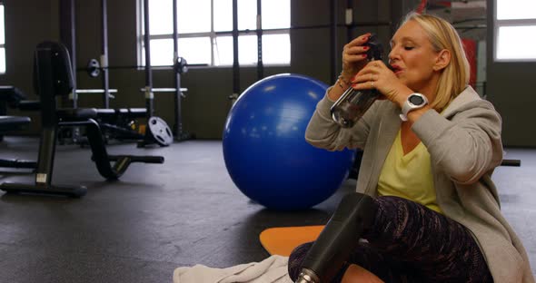 Senior woman drinking water in fitness studio 