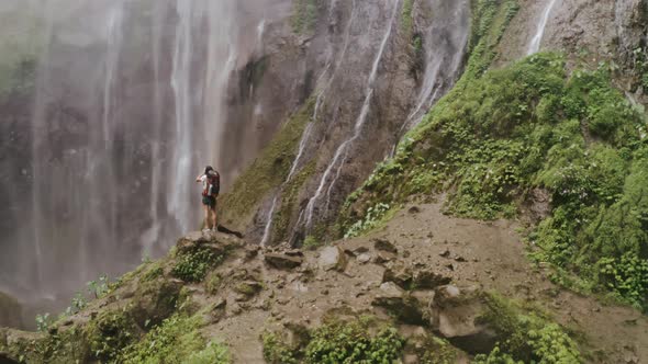 Traveler Woman with Backpack Standing on the Background of a Waterfall
