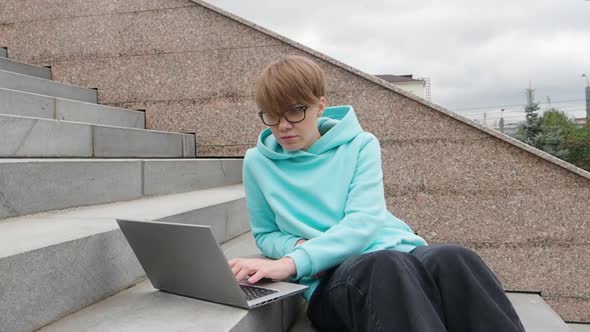 Young Woman with Short Hair is Sitting on Stairs Witl Laptop