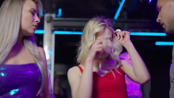 Gorgeous Blond Woman with Blue Eyes in Red Dress Dancing with Group of Friends in Night Club Lights