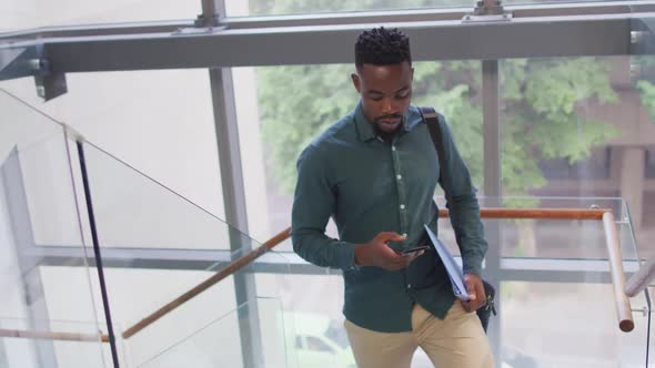 African american businessman using smartphone and holding documents in creative office