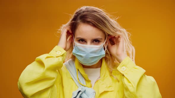 Young Casual Woman Putting on Medical Mask Against Yellow Background