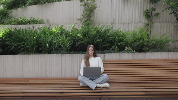 Young Female in Garden Using Laptop Communicates on Internet with Customer