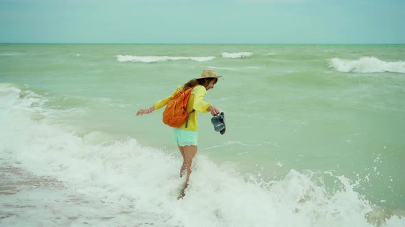 Dreamy Freedom Woman in Summer Bright Clothes with Small Backpack Arms Walking at Seaside Enjoying