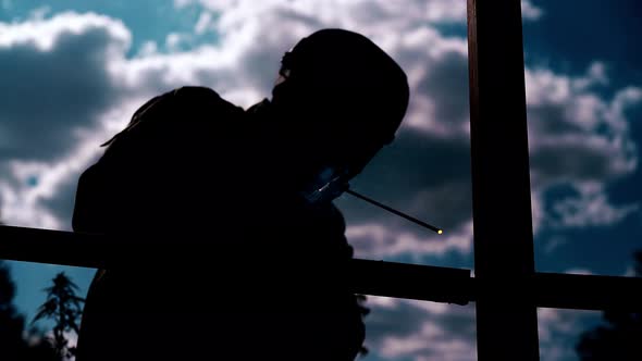 Builder Dark Silhouette with Welding Machine Against Clouds