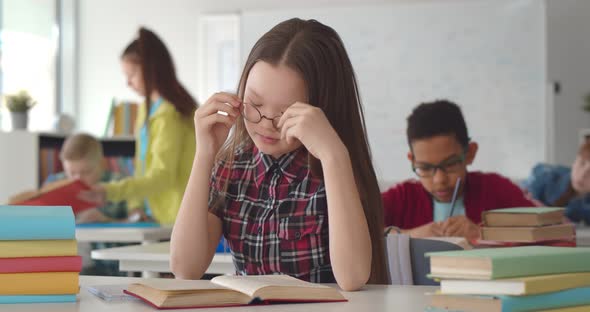 Portrait of Tired and Bored Small Asian Girl Sitting at Desk in Classroom