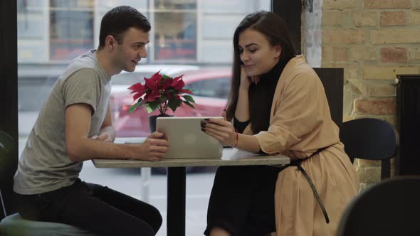 Young Smiling Caucasian Couple Sitting in Cafe Using Tablet