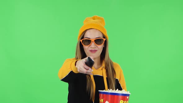 Portrait of Girl in Yellow Hat in 3D Glasses Is Watching TV and Eating Popcorn with TV Remote in Her