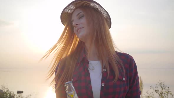 Portrait of Beautiful Hipster Girl Throwing Up Cold Bottle of Beer or Limonade on the Background