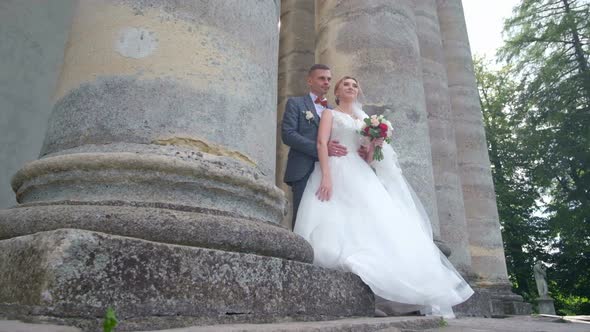 Beautiful Couple of Brides Hugging and Kissing Near Large Columns in the Old Town Wedding Day