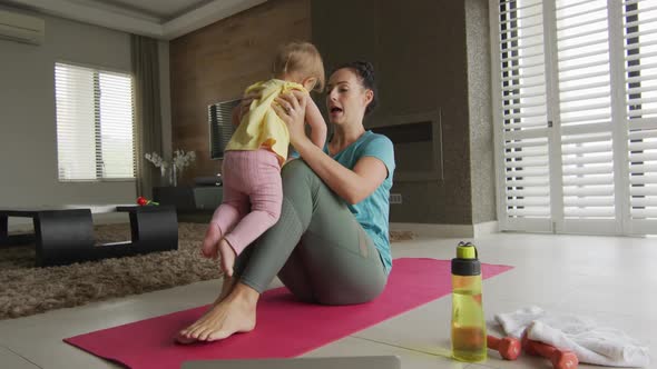 Caucasian mother playing with her baby while practicing yoga on yoga mat at home