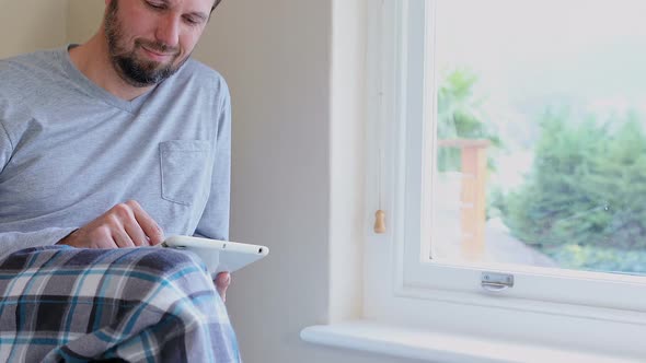 Young man looking out side through window while using tablet 4K 4k