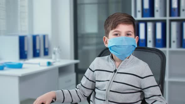 Masked Little Boy Portrait of Patient Sitting in Chair at the Hospital Office Against the Background