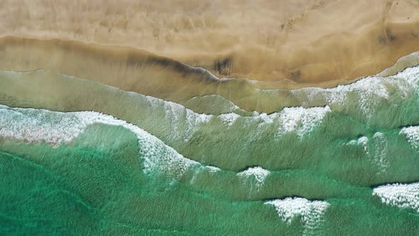 Fly over Kvalvika beach with splashing sea waves