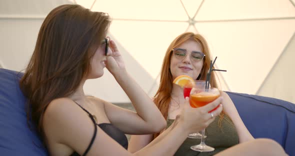 Two Girls in Swimsuits with Cocktails Resting on Bg Chairs