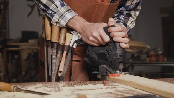 Carpenter is Sawing a Wood Plank with Electric Jig Saw Machine in Carpentry Workshop