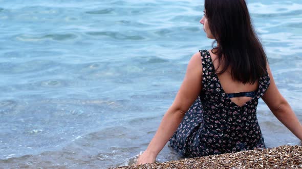 A beautiful sexy young girl sits on the shore of the ocean and looks into the distance.