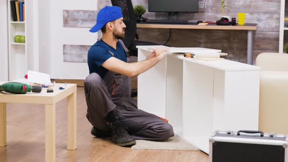 Zoom in Shot of Man in Overalls Assembles a Shelf