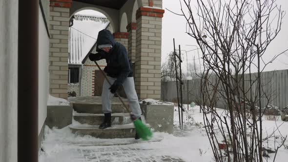 Man sweeps snow from stairs near house in winter