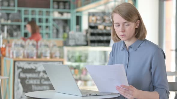 Young Woman Reading Documents While Using Laptop