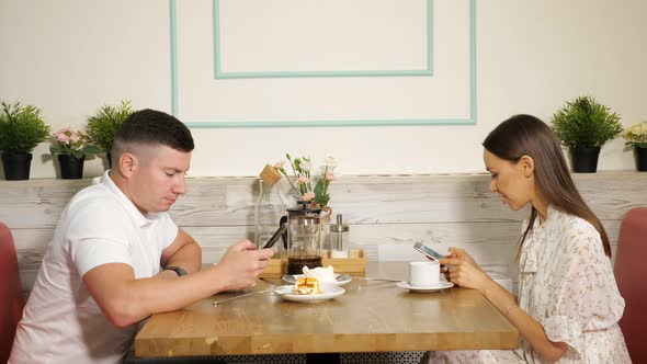 Man and Woman Use Phones at Table with Desserts in Cafe