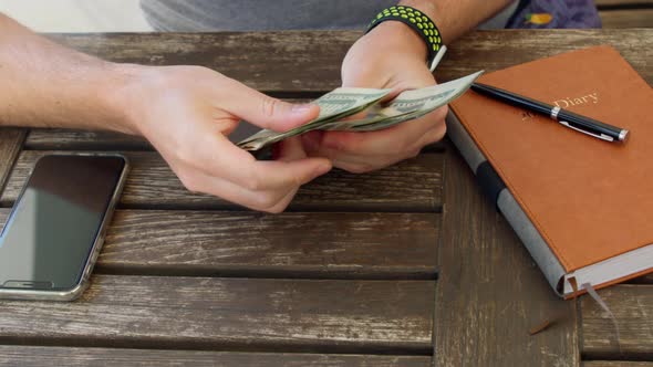 Man Counts Twentydollar Cash Banknotes on Wooden Desk