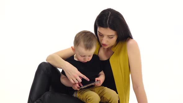 Girl Tells and Shows Something on the Smartphone To Her Child. White Background