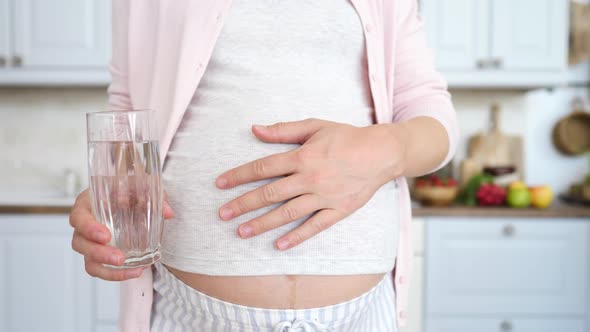 Pregnant Woman Holding Glass Of Water In Kitchen.