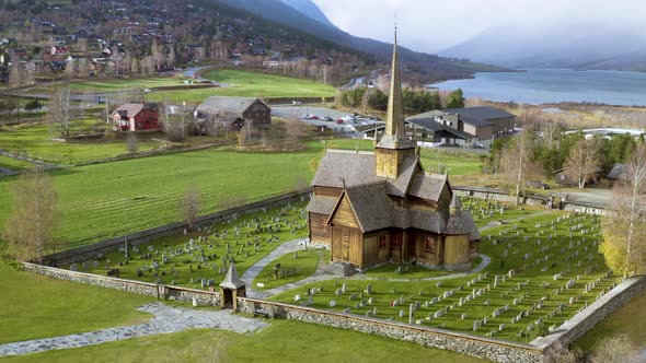 Beautiful Wooden Stave Church Of Lom Surrounded By Mountains And Trees In Norway - aerial drone shot